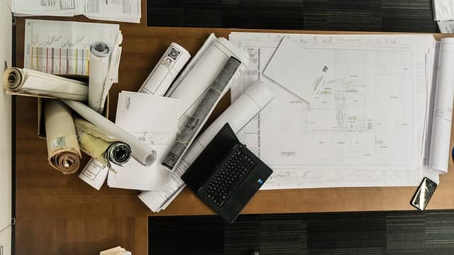 Photos of a desk littered with detailed architecture plans. Big Design Up Front is a lot of speculative work