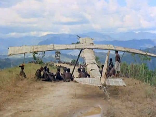 A photo of people sitting in front of a 'Cargo Cult' wooden plane