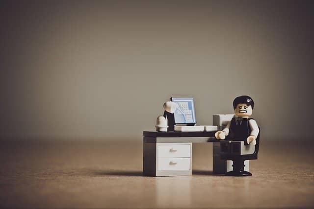 A lego character at his desk looking stressed out by too much work. Spending many weeks to test a legacy code bug is not justifiable.