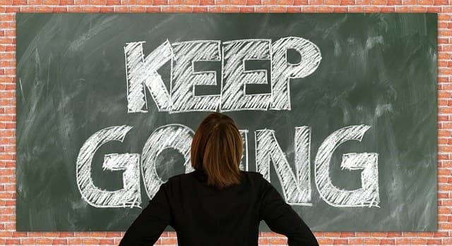 A photo of someone standing in front of a black board with "Keep Going" written on it. Succeeding to sell your technical coaching services internally is mostly of matter the finding the way to do so, keep going until you find how!