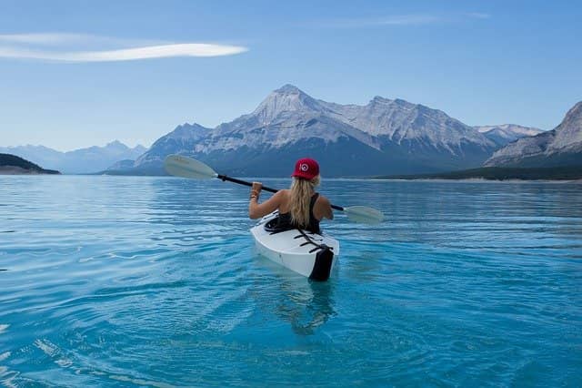 Photo taken from behind of a women in a kayak on a lake surrounded by mountains. Running a code retreat of mobbing experiment is a way to explore and discover new ways of working.