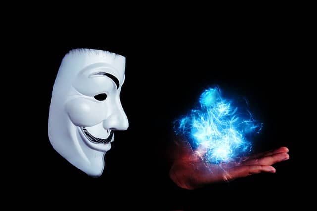 Illustration of an Anonymous Mask holding shining and twirling shapes in their hands. It looks as if they are blowing to create change.