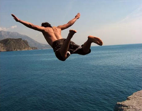 A guy jumping from a cliff into the sea