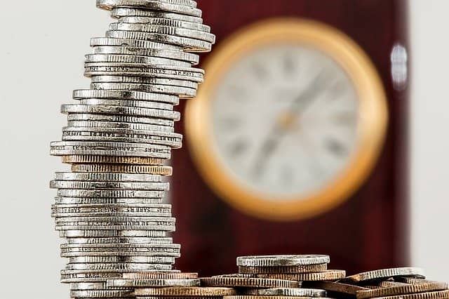 Photo of a pile of coins with a clock in the background. Like compounding in finance, the small but repeated benefits of mob programming create a huge payback in the long term