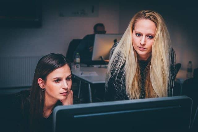 Photo of 2 person pairing in front of a computer. Part-time coaches not only help us to coach other teams, but they also stay as full-time embedded coaches in their own teams! This is what makes change stick.