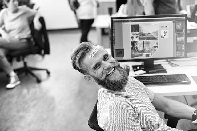 Photo of a man smiling and sitting at his desk in an open space. Spend the minimum time with the laggards and focus on enthusiastic people instead.