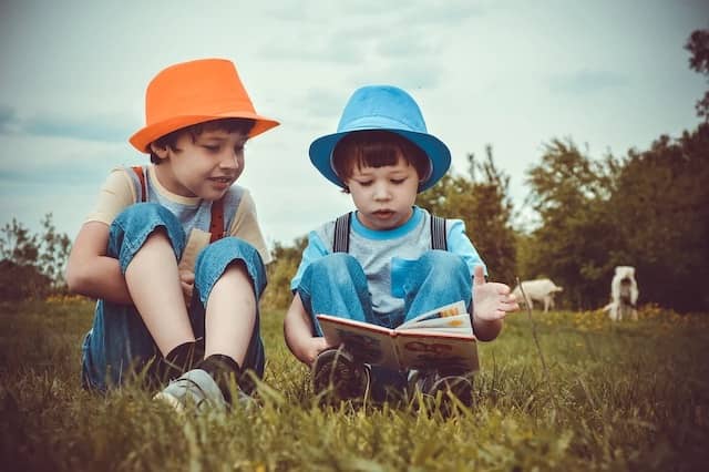 Photo of 2 kids sitting in the grass. One is reading while the other is listening. Listening to coachees is the first step to fix the 'It does not work in real life!' comment.