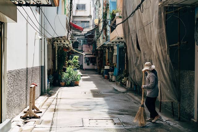 Photo of a small city alley, where we can see a woman sweeping in front of her house.