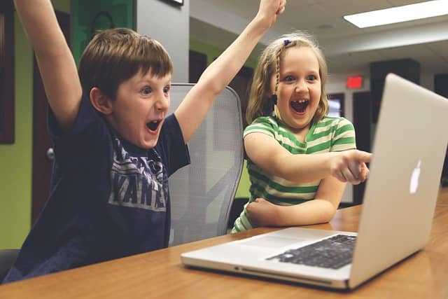 Photo of 2 kids having fun and claiming victory in front of a computer. Good communication skills have more chance to spread contagious happiness in the workplace.