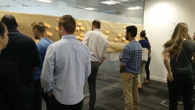 Photo of people during and Event Storming Workshop. We can see many people engaged in discussion in front of the "Infinite design board" typical to Event Storming